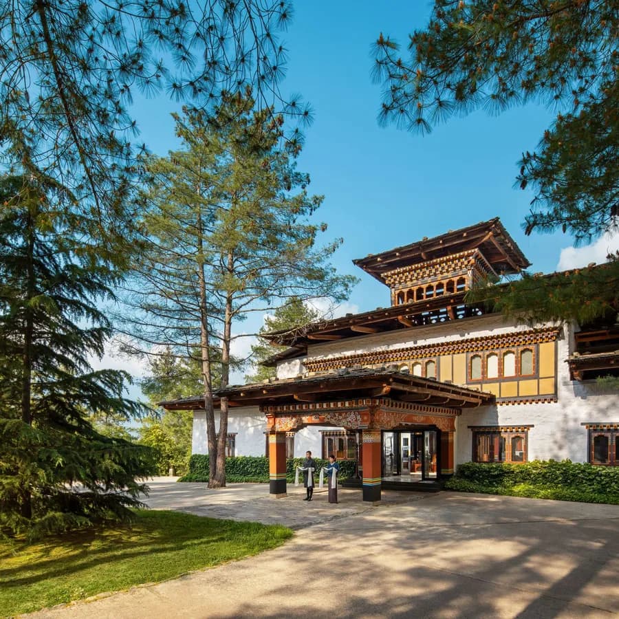 Entrance of a luxury resort built in traditional Bhutanese architecture, with staff offering a welcome scarf