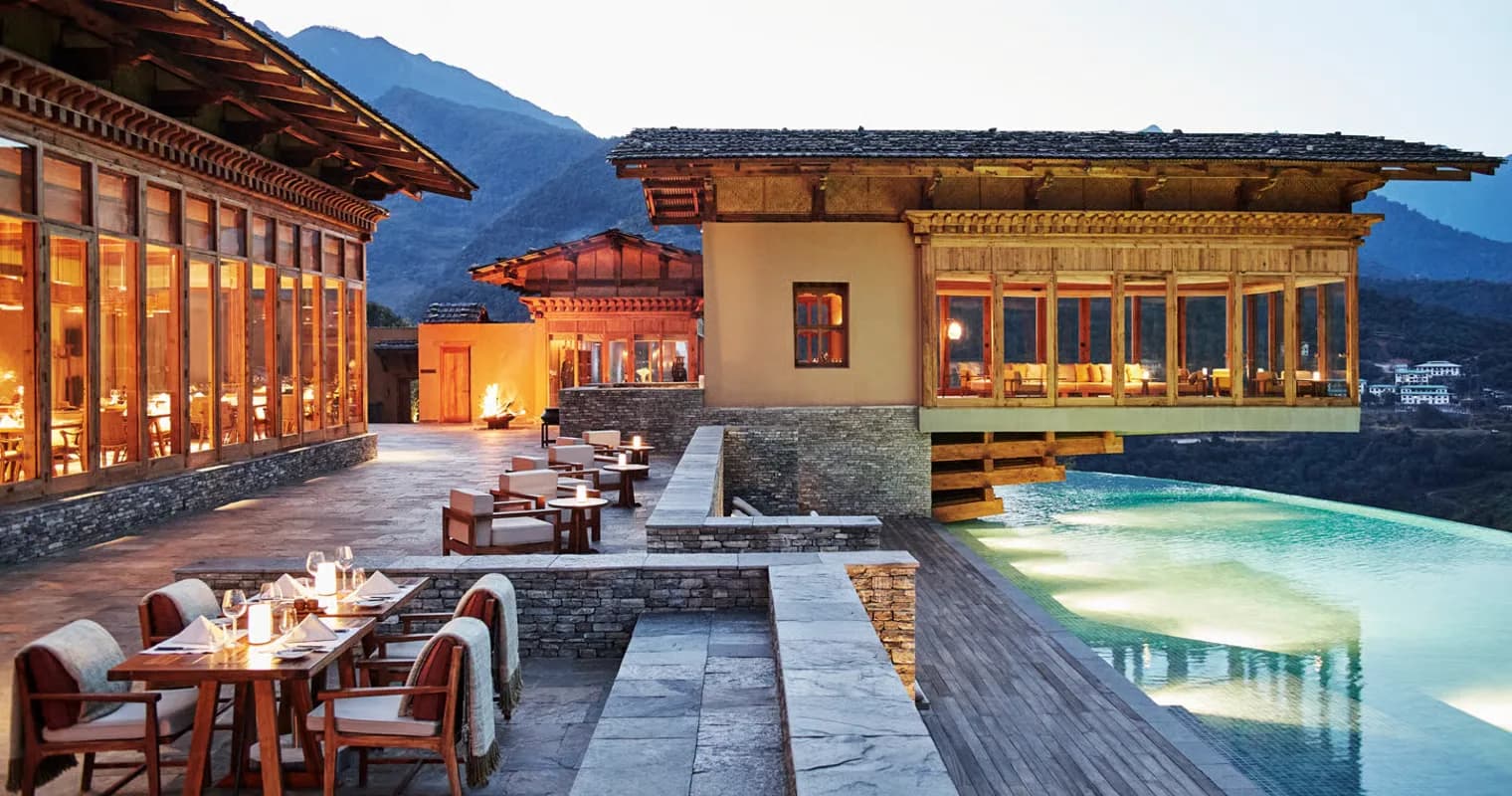 Terrace and infinity pool of a luxury Bhutanese resort at dusk, framed by Himalayan mountains