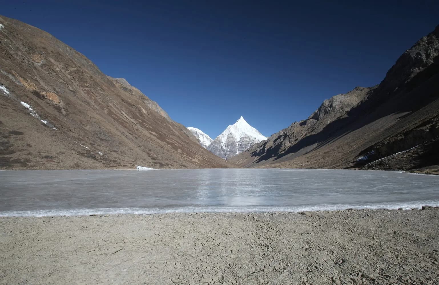 Frozen alpine lake below a snow peak on the Dagala Thousand Lakes trek