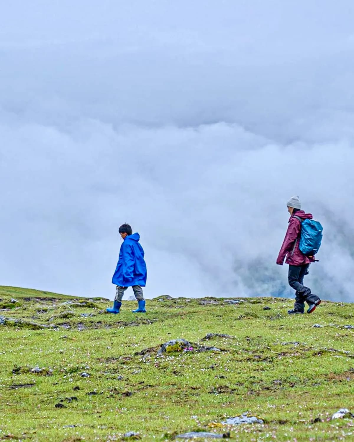 A trekker and a child walking a high alpine ridge above a sea of clouds