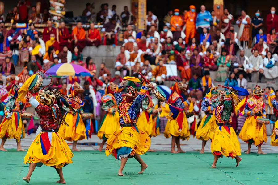 Colorful Bhutan festival with monks in vibrant masks performing a sacred masked dance at a traditional monastery.